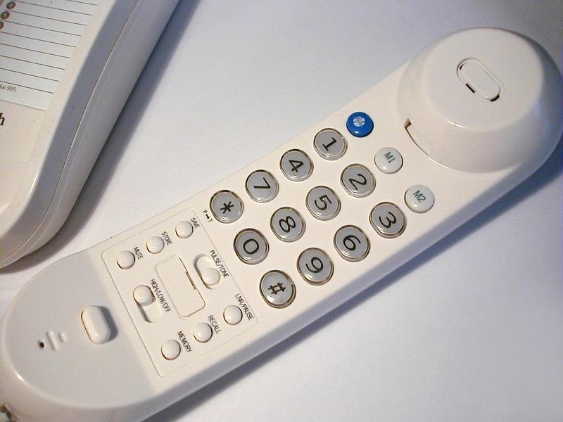 Free Stock Photo: White handset of a land line telephone off the hook lying on a white surface with the keypad uppermost