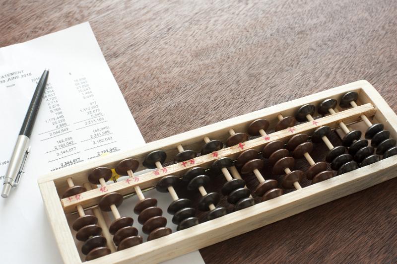 Free Stock Photo: Wooden abacus being used for accounting lying on a desk with a balance sheet and ballpoint pen viewed from above