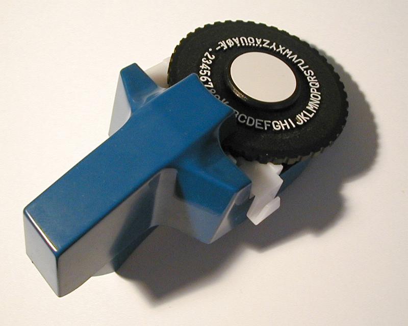 Free Stock Photo: Dymo machine for printing embossed labels on tape with its alphanumeric wheel lying on white with shadow