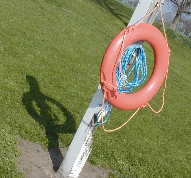 Free Stock Photo: Red lifesaver or life ring hanging on a pole with attached blue rope for use as a flotation device in the rescue of a drowning person