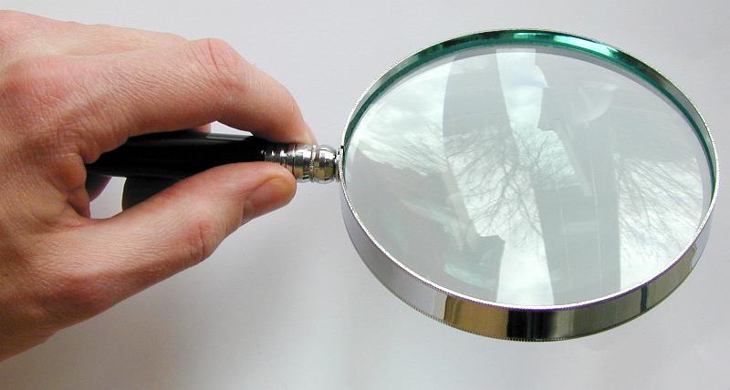Free Stock Photo: Man holding a round magnifying glass with a reflection on the lens over a blank sheet of white paper, high angle view