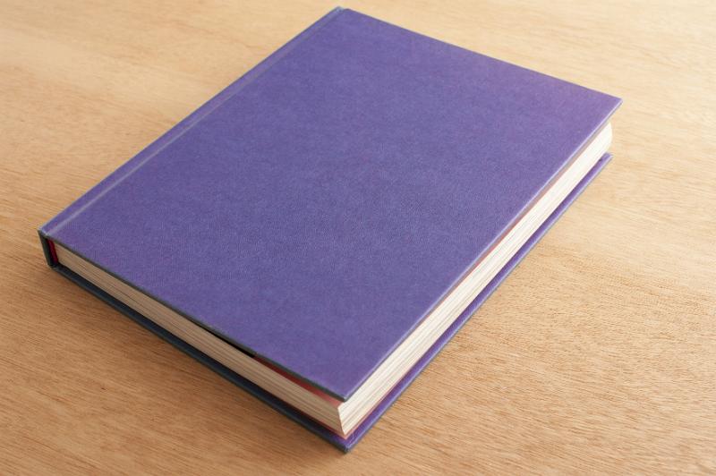 Free Stock Photo: Closed hardcover notebook with a purple cover lying diagonally on a wooden desk in a close up view with copy space