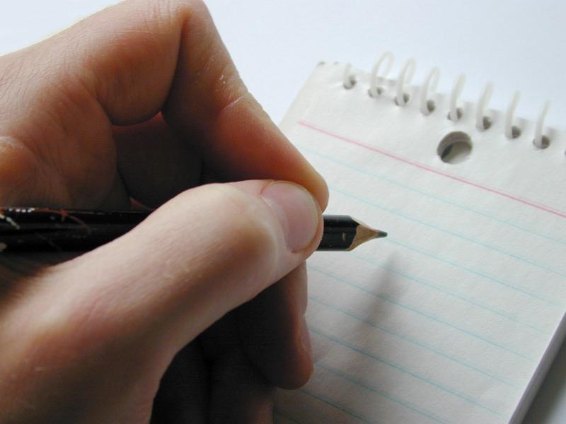 Free Stock Photo: Man writing on a spiral bound notepad holding the pencil poised above the blank white ruled page, close up on his fingers