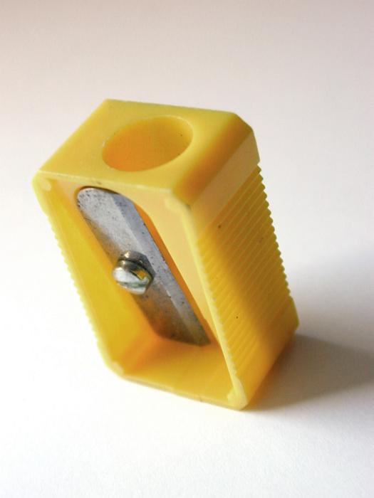 Free Stock Photo: Yellow plastic pencil sharpener standing upright on white with the blade towards the camera