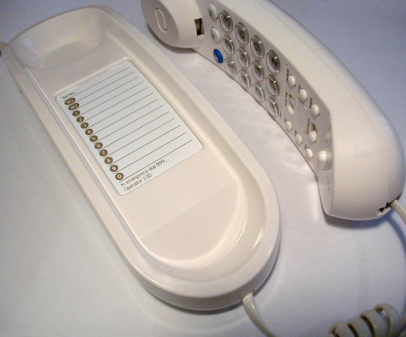 Free Stock Photo: Land line telephone instrument with the receiver off the hook lying alongside it on a white surface, close up view