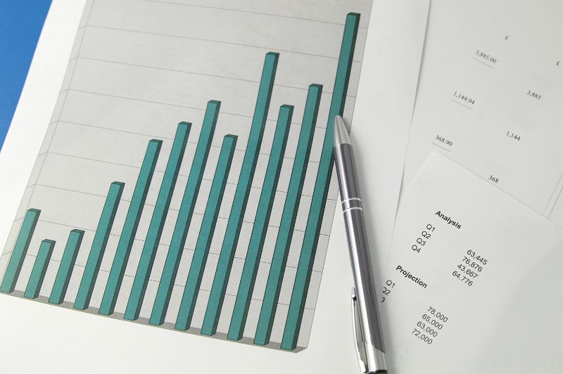 Free Stock Photo: Overhead view of a bar graph charting data and tables of statistics with a metallic silver pen