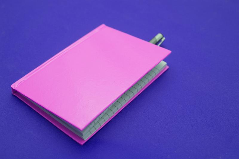 Free Stock Photo: Closed pink notebook with pen inside on purple background