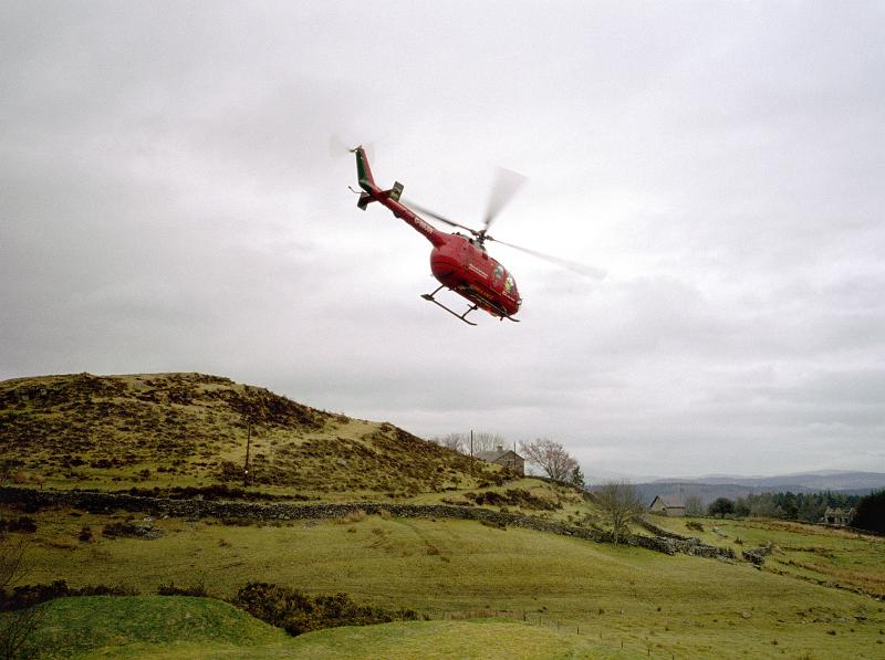 Free Stock Photo: Air ambulance helicopter flying low over lush green hilly terrain against an overcast sky as it flies to collect a patient for transport to hospital