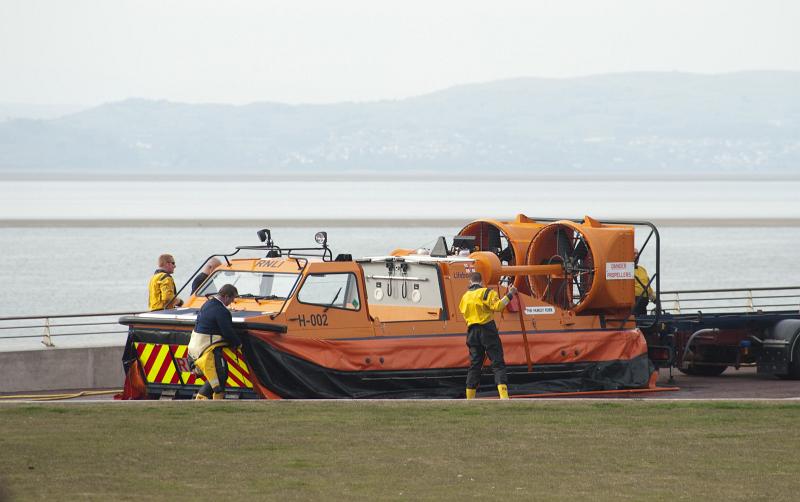 Free Stock Photo: Men working on a coastguard hovercraft which is standing onshore above a sandy shallow bay
