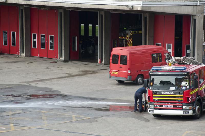 Free Stock Photo: A fireman performs maintenance on a fire engine parked on the tarmac in a fire station courtyard