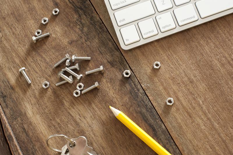 Free Stock Photo: nuts and bolts on a wooden desk with the corner of a computer keyboard and yellow pencil