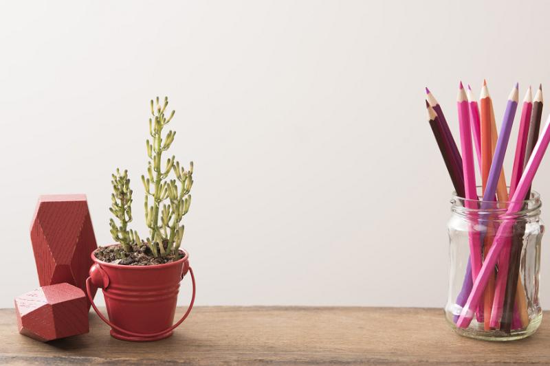 Free Stock Photo: Plant growing in short red pail on wood table beside mason jar filled with colored pencils